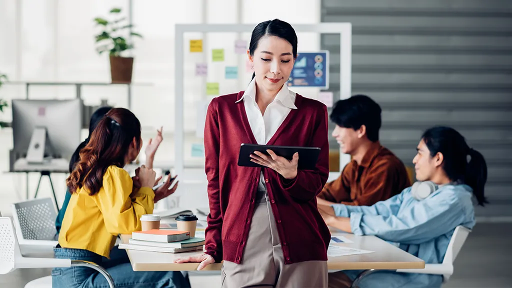 A woman reviewing notes on a tablet during a group discussion in a modern classroom, representing learners exploring SkillsFuture SCTP courses.