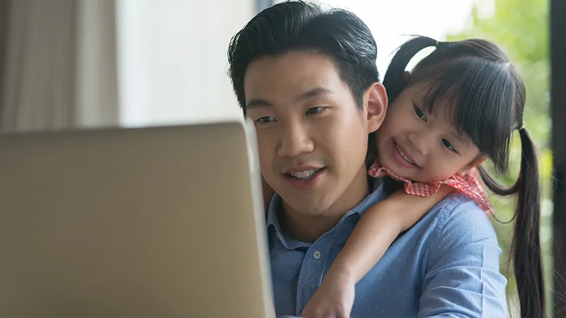 A father studying on his laptop with his daughter hugging him while figuring out if it is too late to change career or upskill